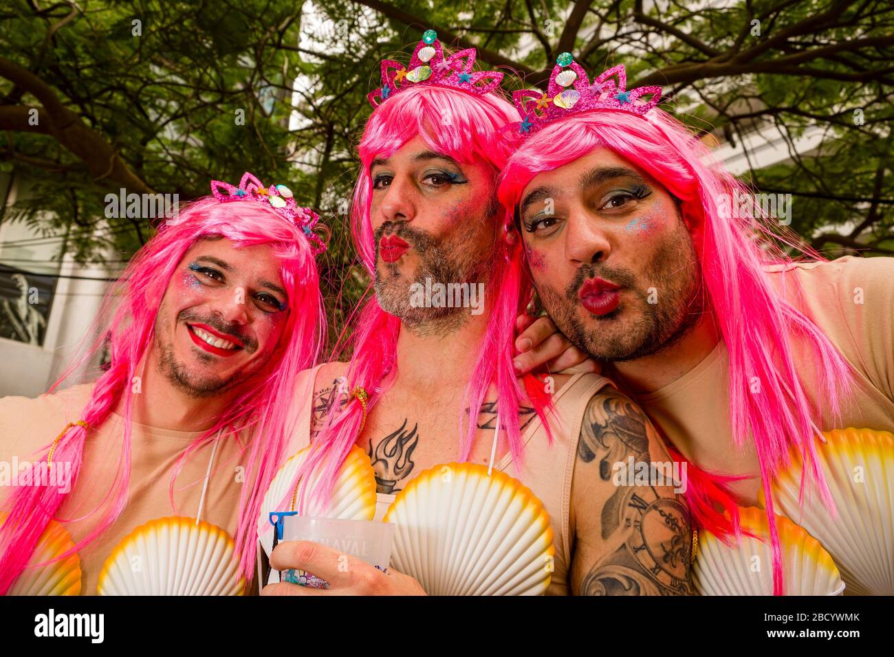 Eine Gruppe von Männern, die sich als Frauen verkleidet haben, rosa Perücken tragen und lächeln, während des Karnevals tagsüber auf den Straßen feiern Stockfoto