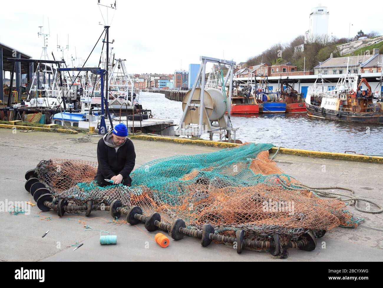 Ein Fischer repariert Netze am North Shields Fish Quay am Ufer des Flusses Tyne in Nordostengland. Da die Exportmärkte nach Europa und China ruiniert sind, Restaurants und Chippies geschlossen sind, die Gastlichkeit geschlossen ist und viele Supermärkte ihre Fischzähler nicht besetzen, haben die Skipper beschlossen, ihre Schiffe zusammengebunden zu halten. Stockfoto