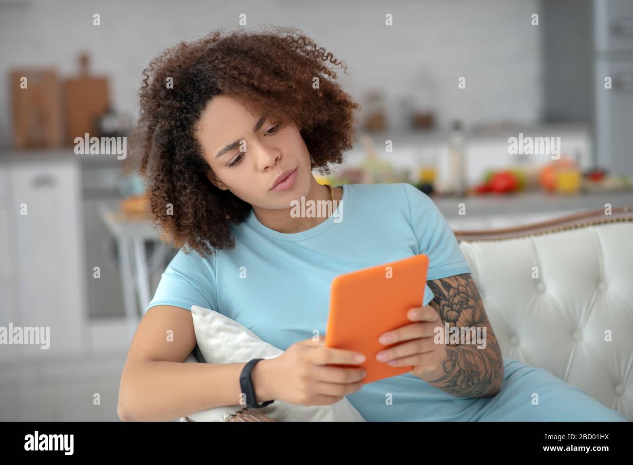 Ernsthafte Frau, die auf einer Couch sitzt und auf eine Tablette blickt. Stockfoto
