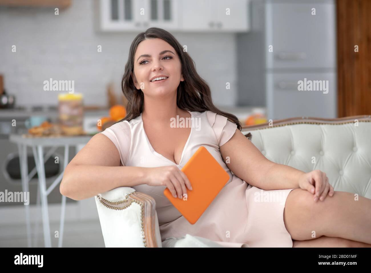 Junge Frau in hellem Kleid mit Tablette auf dem Sofa. Stockfoto