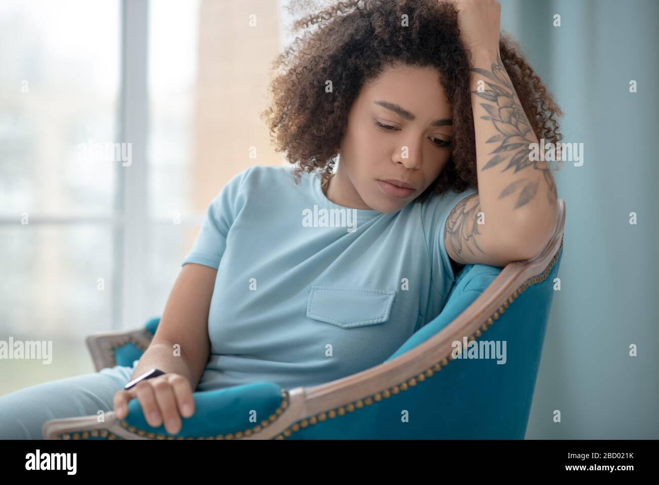 Frau, die seitlich in einem Sessel sitzt und nach unten blickt. Stockfoto