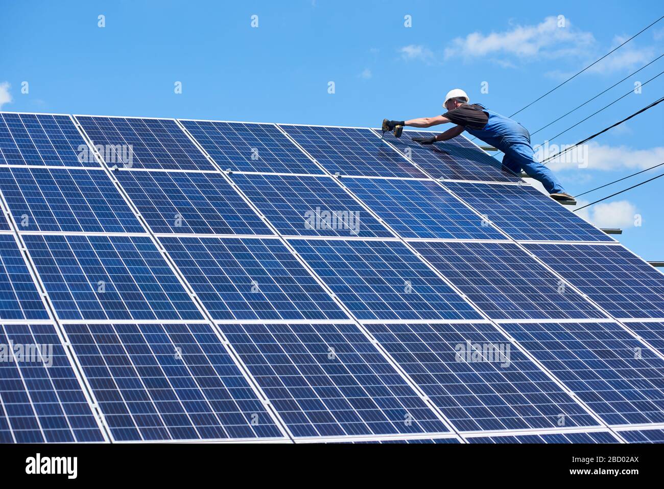Facharbeiter, die Solarpaneele auf der grünen Metallkonstruktion installieren, verwenden verschiedene Geräte und tragen Helm. Innovative Lösung für die Energielösung. Nutzung erneuerbarer Ressourcen. Grüne Energie. Stockfoto