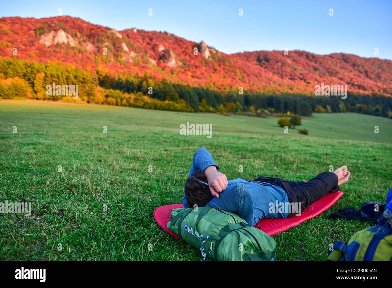 Touristen entspannen sich auf der Herbst-Abendwiese, bunte Bäume im Hintergrund Stockfoto