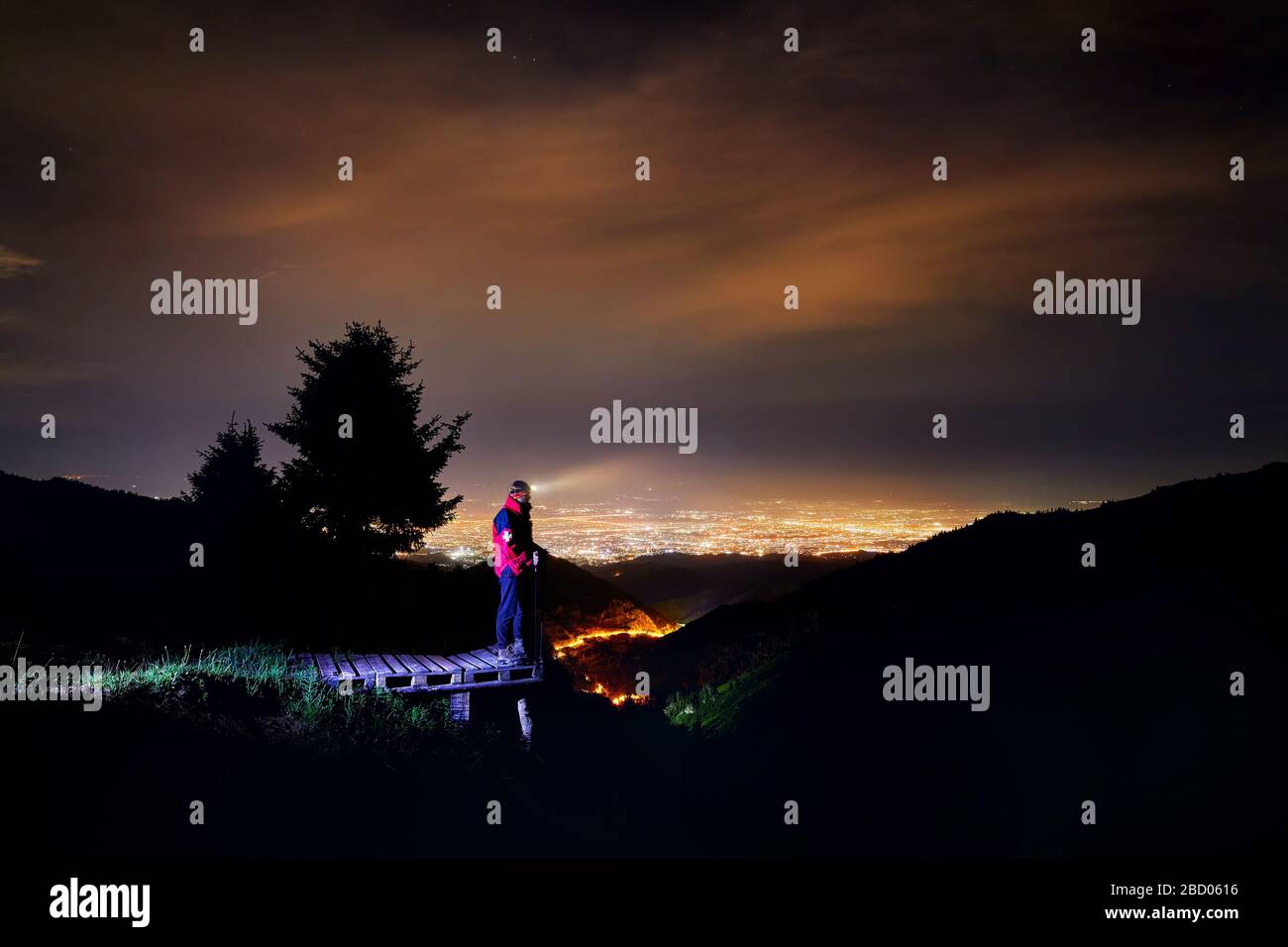 Rettungsschwimmer im roten Mantel mit medizinischen Kreuz und Fernlicht der Scheinwerfer in der Mountain Ski Resort mit Blick auf die Nacht City Light Stockfoto