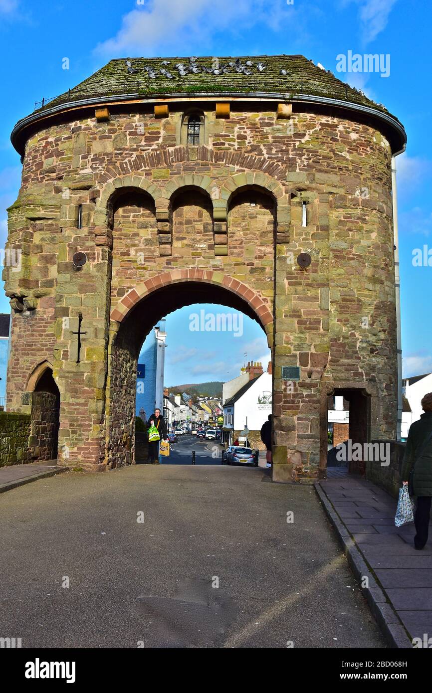 Der Turm und Torbogen auf der Brücke über den Fluss Monnow am Rande der Stadt Monmouth.Blick auf die wichtigsten Geschäfte auf Monnow Street durch Stockfoto