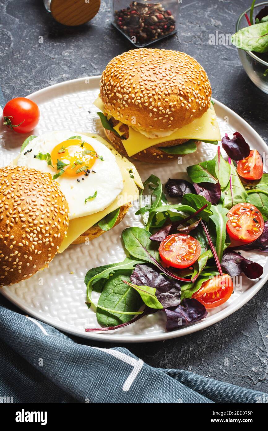 Frühstück zwei Burger mit Huhn, frittiertem Ei und Käse auf dunklem Steingrund Stockfoto