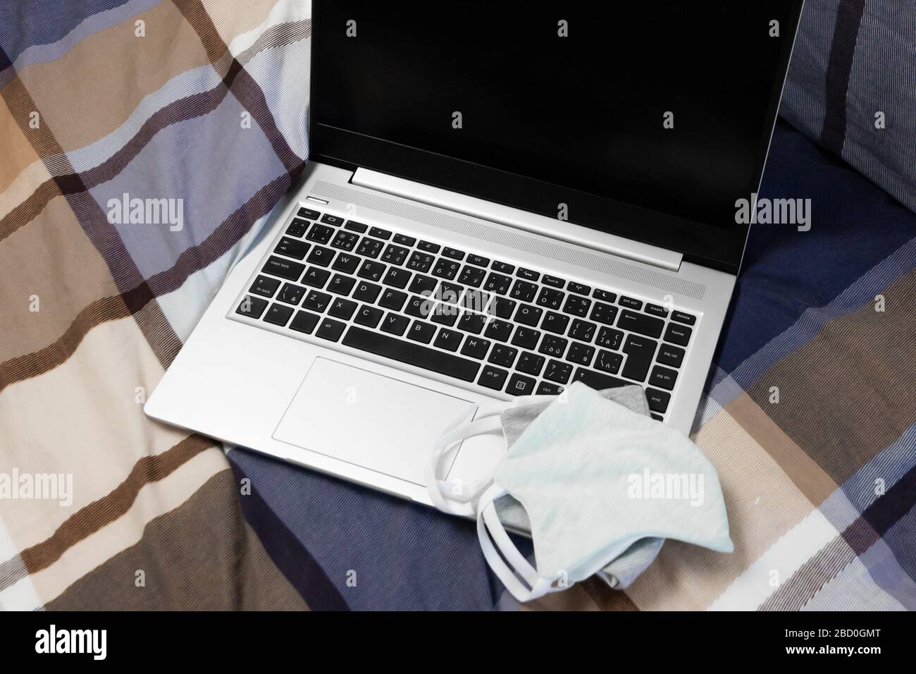 Draufsicht auf einen Laptop im Bett und Schutzmasken darauf. Konzept der Sicherheitsarbeit zu Hause bei einer Pandemie von Coronavirus. Stockfoto Draufsicht auf einen Laptop im Bett und Schutzmasken darauf. Konzept der Sicherheitsarbeit zu Hause bei einer Pandemie von Coronavirus. Stockfoto