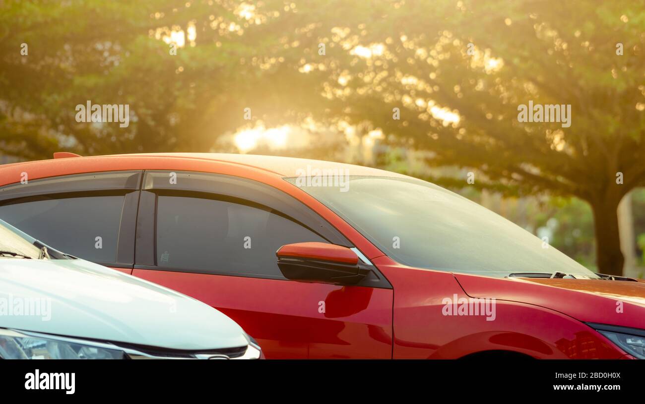 In der Nähe geparktes rotes SUV-Auto auf dem Parkplatz des Einkaufszentrums oder Büros im Freien. Luxusauto parkt in der Nähe des grünen Baums auf dem Parkplatz mit dem Morgen Stockfoto