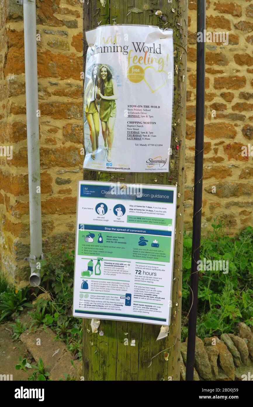 Kontrastierende Schilder auf dem Pfosten im Dorf Oxfordshire von Hook Norton. Eine Werbe-Schlankheits-Welt und die andere geben Ratschläge zu Coronaviru Stockfoto