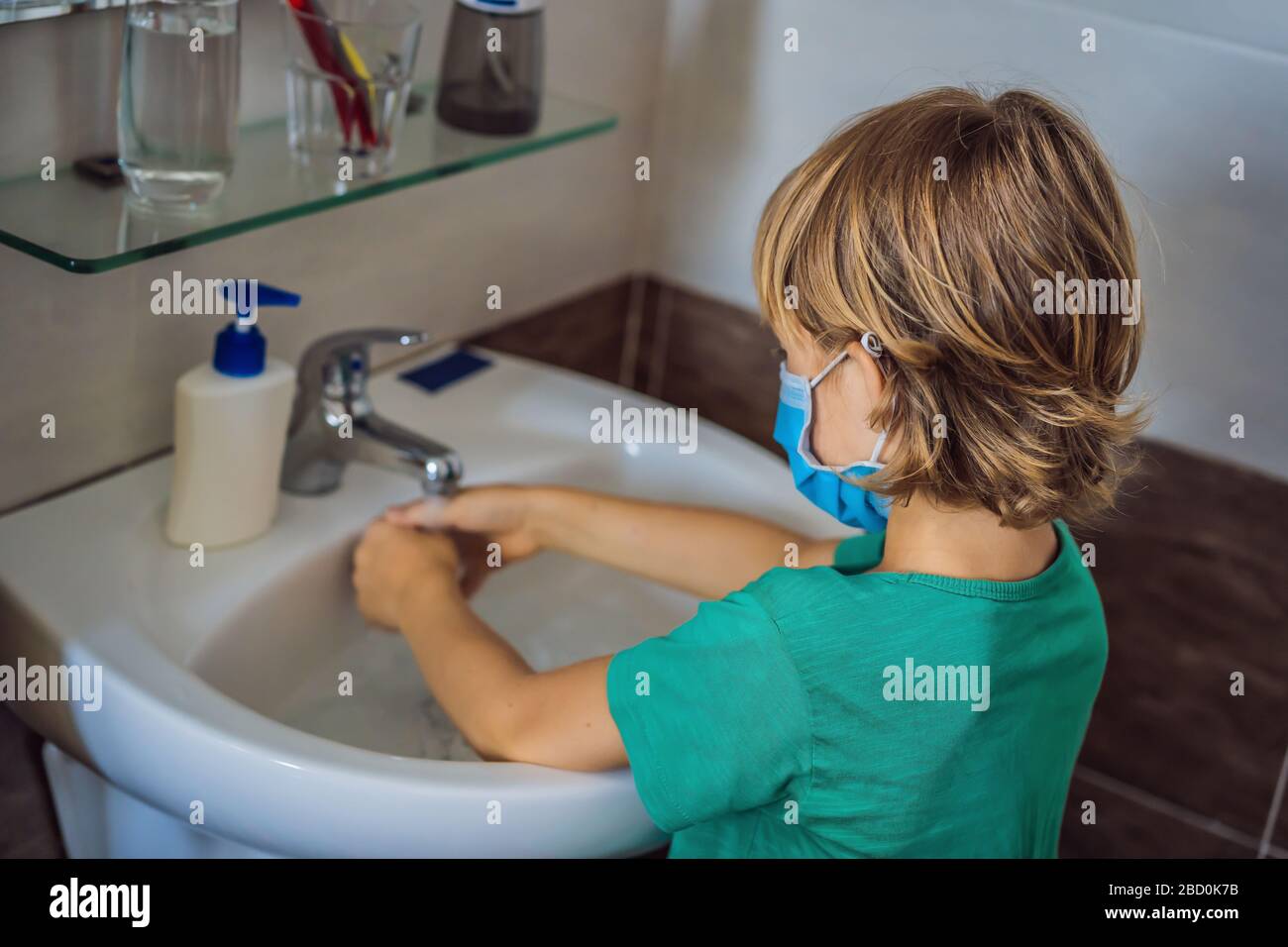 Der Junge wäscht seine Hände mit Seife. Junge in einer medizinischen Maske wegen Coronavirus. Pandemie. Bleiben Sie zu Hause. Waschen Sie Ihre Hände Stockfoto