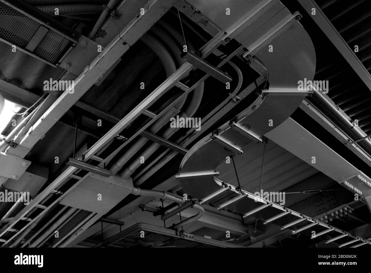 Monochromes Foto von Stromverteilungs- und Sanitäranlagen an der Decke einer Industrieanlage mit komplexer Struktur Stockfoto