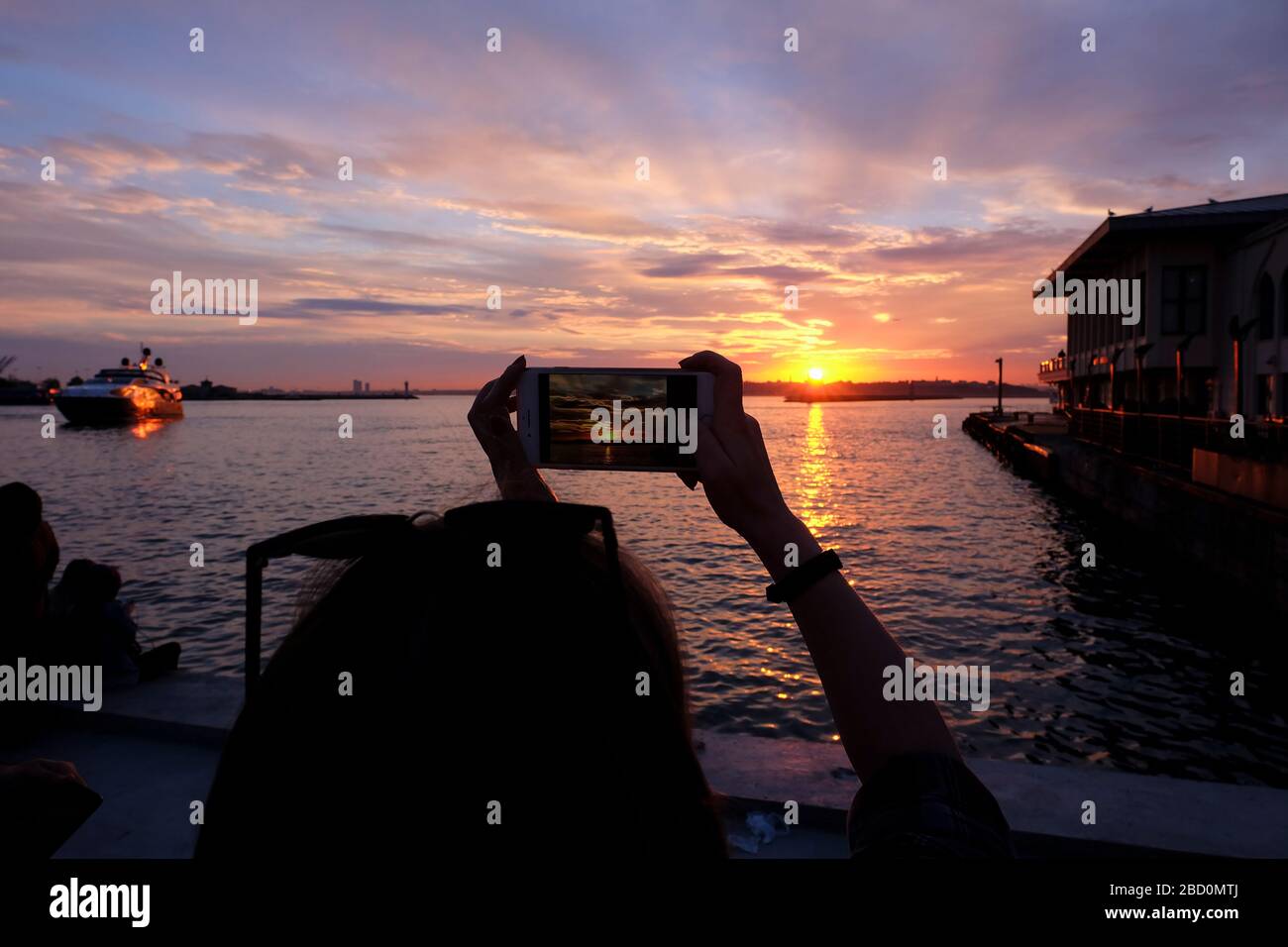 Junge Frau fotografiert mit einem Smartphone an der Küste von Istanbul, Kadikoy bei Sonnenuntergang. Stockfoto