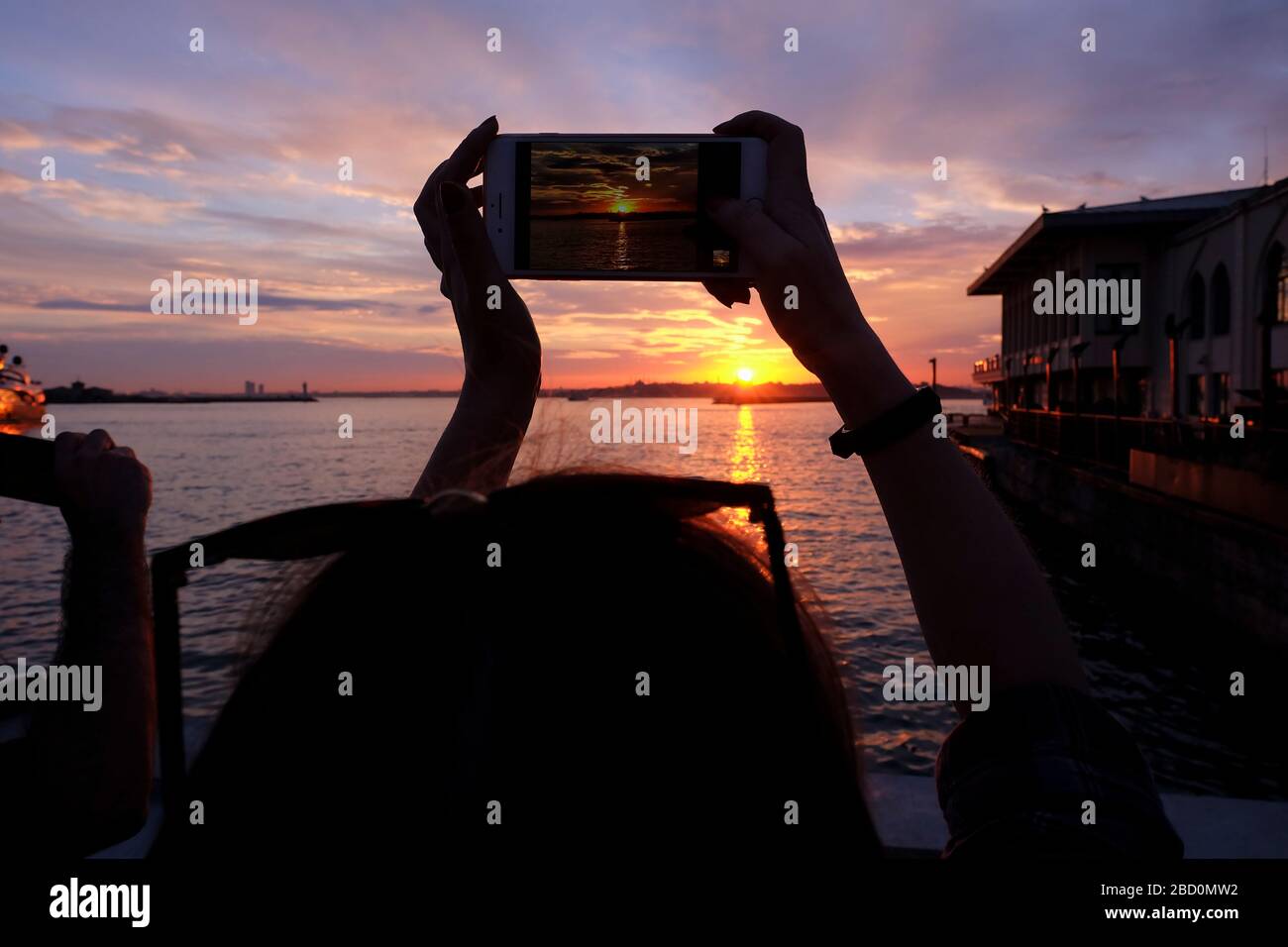 Junge Frau fotografiert mit einem Smartphone an der Küste von Istanbul, Kadikoy bei Sonnenuntergang. Stockfoto