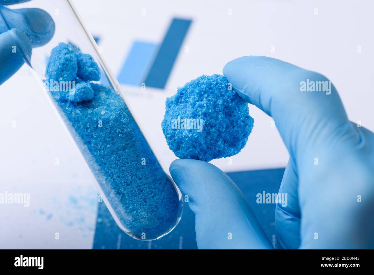 Blaues Kristallmaterial in der Hand und Glasprüfrohr im Laborforschungskonzept Stockfoto