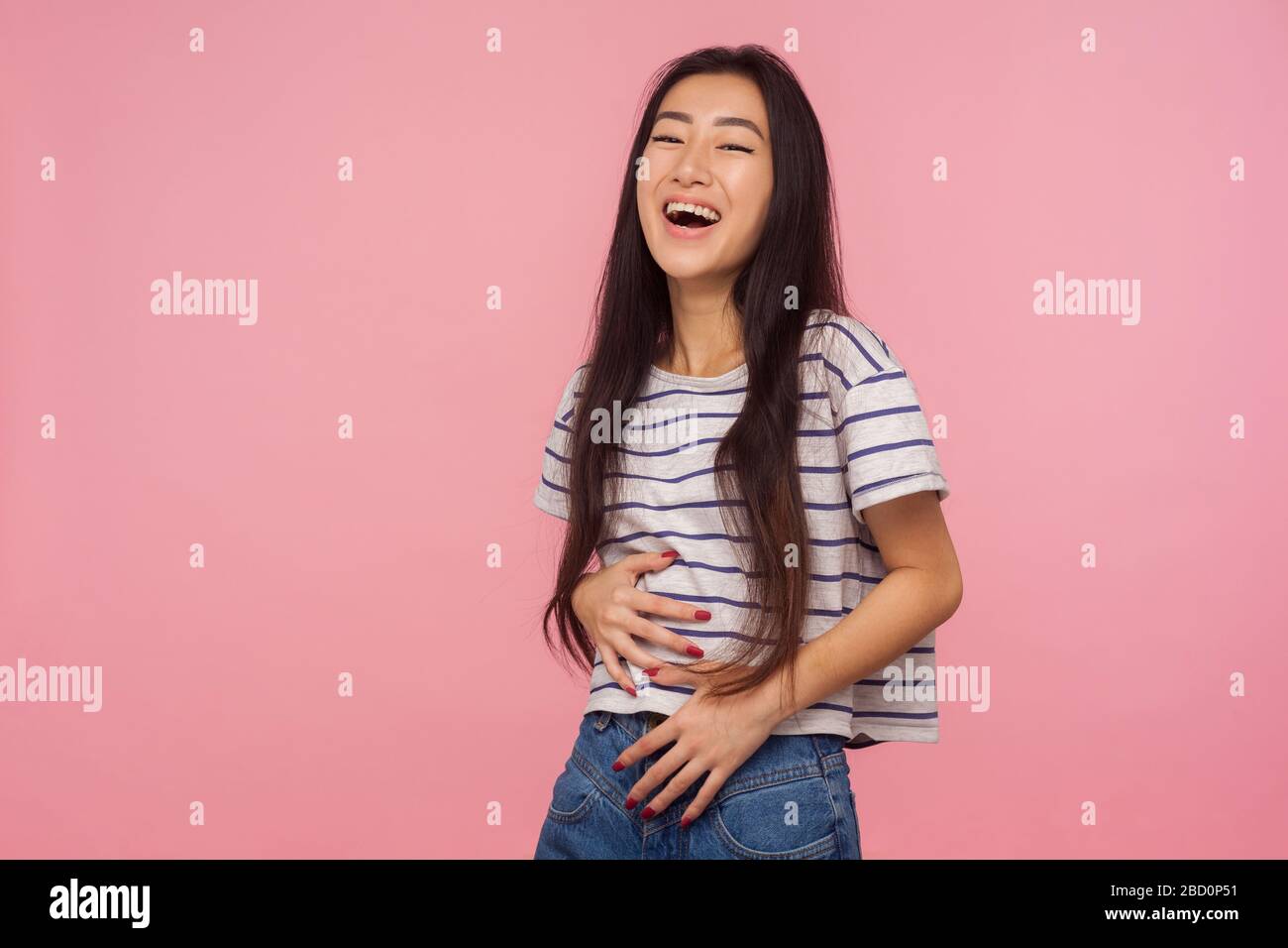 Witziger Witz! Porträt eines fröhlichen optimistischen Mädchens mit langen Haaren im gestreiften T-Shirt, das Bauch hält und laut lacht, amüsiert von albern lustigen Anecdot Stockfoto
