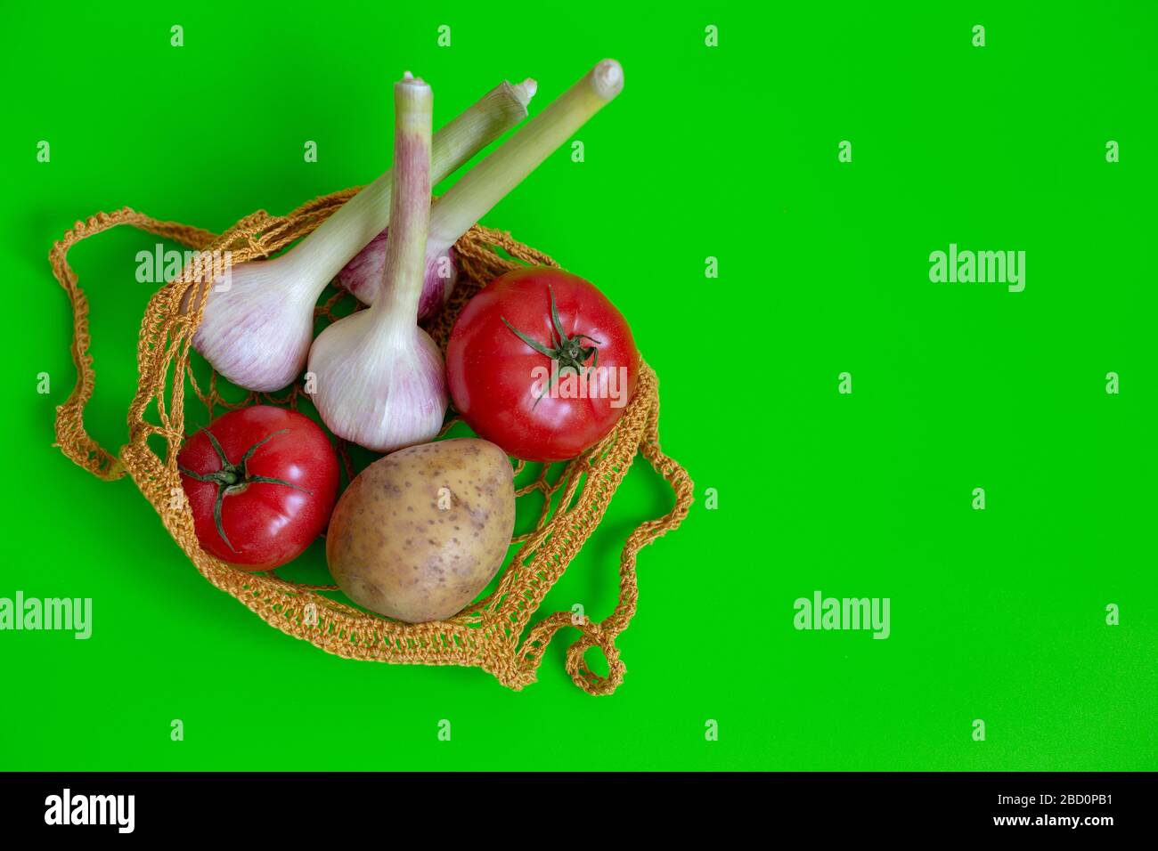 Stricktasche auf grünem Tisch mit Gemüse: Tomaten, Knoblauch, Kartoffeln. Vegetarisches Gemüse. Gesunde Ernährung. Ansicht von oben. Kopierbereich Stockfoto