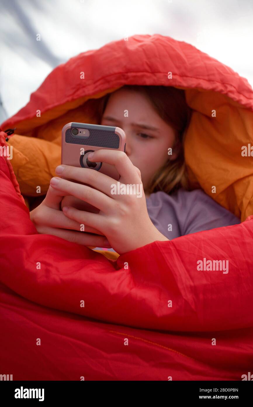 Junges Mädchen in ihrem roten Schlafsack, das ihr iPhone beobachtet Stockfoto
