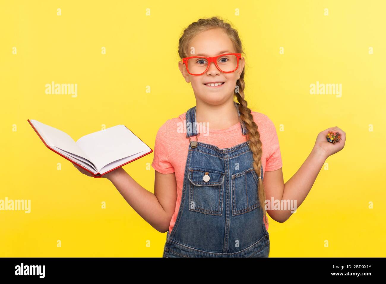 Kreatives Lernkonzept. Portrait des cleveren kleinen Mädchens in einer Brille mit Notizbuch und Bleistiften, Kind lächelt an der Kamera und genießt eine interessante Ausbildung Stockfoto