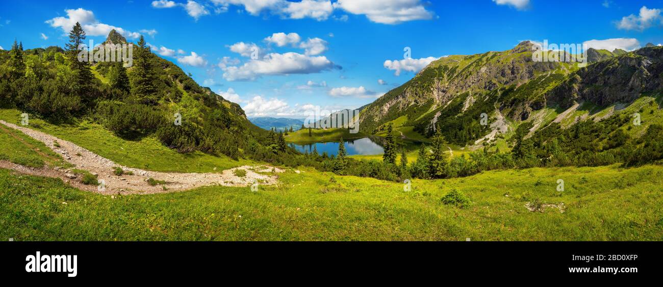 Herrliche Bergkette rund um einen See, mit tiefblauem sonnigen Himmel und grünen Wiesen im Vordergrund Stockfoto