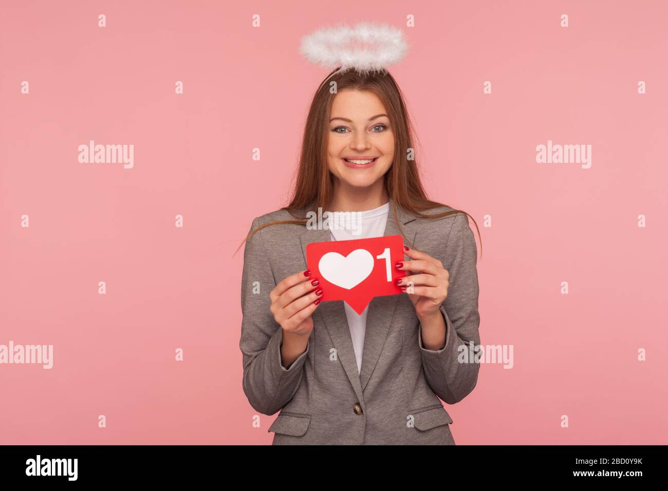 Porträt einer liebenswerten brünetten Frau mit Nimbus im Business-Anzug, die das Herz des Netzwerks wie Ikone hält und mit einem Lächeln auf die Kamera lächelt, und empfiehlt, dem Blog zu folgen. i Stockfoto