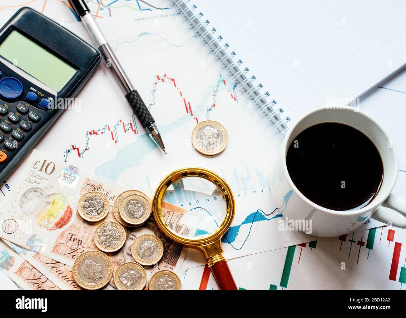 Einige Geldrechner (Pfund, Pfund), eine Kappe Kaffee, Lupe und verschiedene Geldkarten auf dem Tisch. Ansicht von oben. Getont Stockfoto