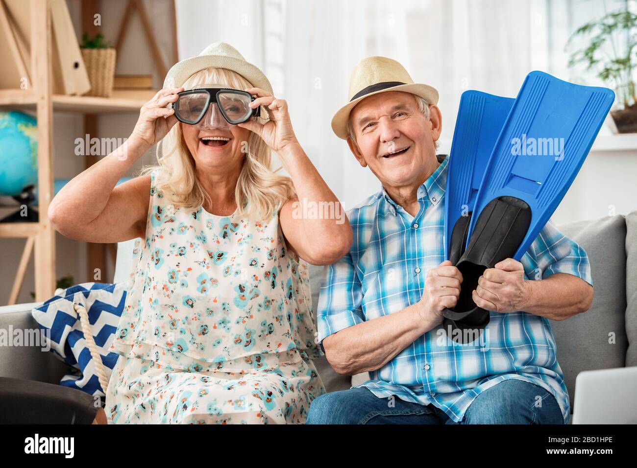 Ein älteres Paar sitzt im Reisebüro und trägt eine Schwimmmaske und Flossen und lacht fröhlich Stockfoto