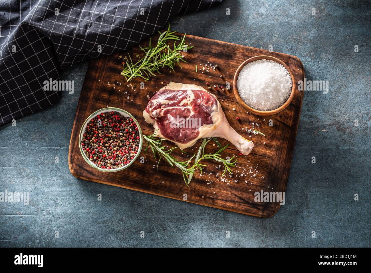 Blick auf den Fleischpräparat in einer dunklen rustikalen Umgebung. Unbehacktes Geflügelbein, frischer Rosmarin, Pfeffercorn und Salz auf dunkelbraunem Schneidebrett Stockfoto