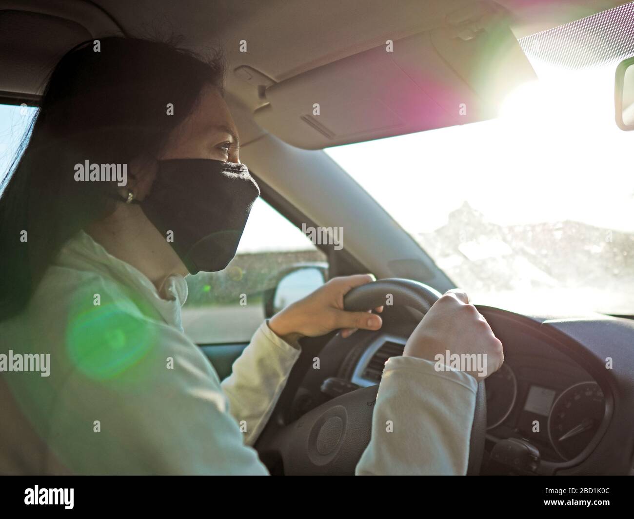 Frau mit Schutzmaske auf dem Gesicht, die während einer Coronavir-Pandemie mit dem Auto fährt Stockfoto