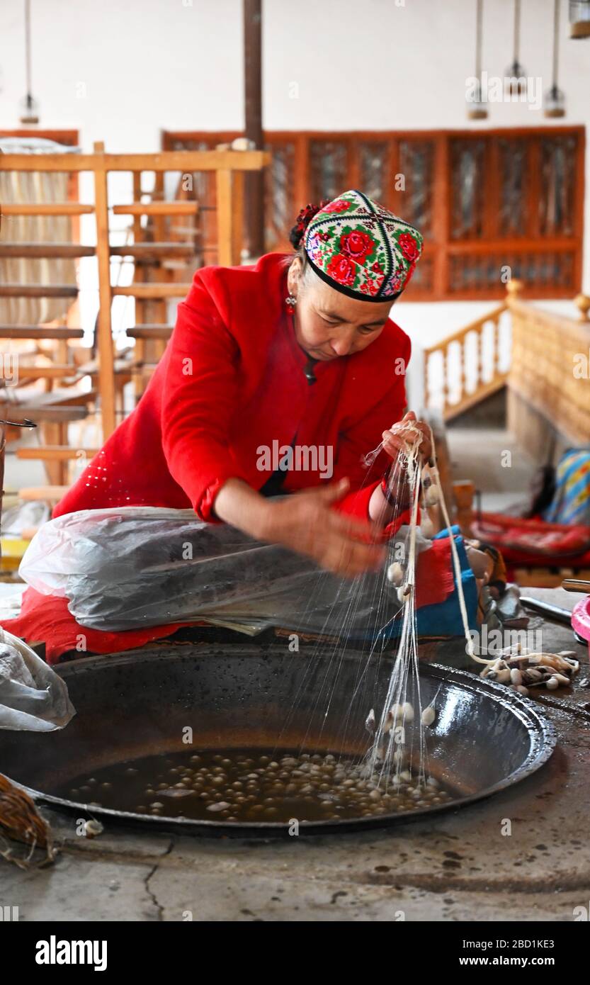 Uyghurfrau spinnt Seidenfaden aus Kokonen in der traditionellen Seidenwerkstatt Jiya, Xinjiang, China, Asien Stockfoto