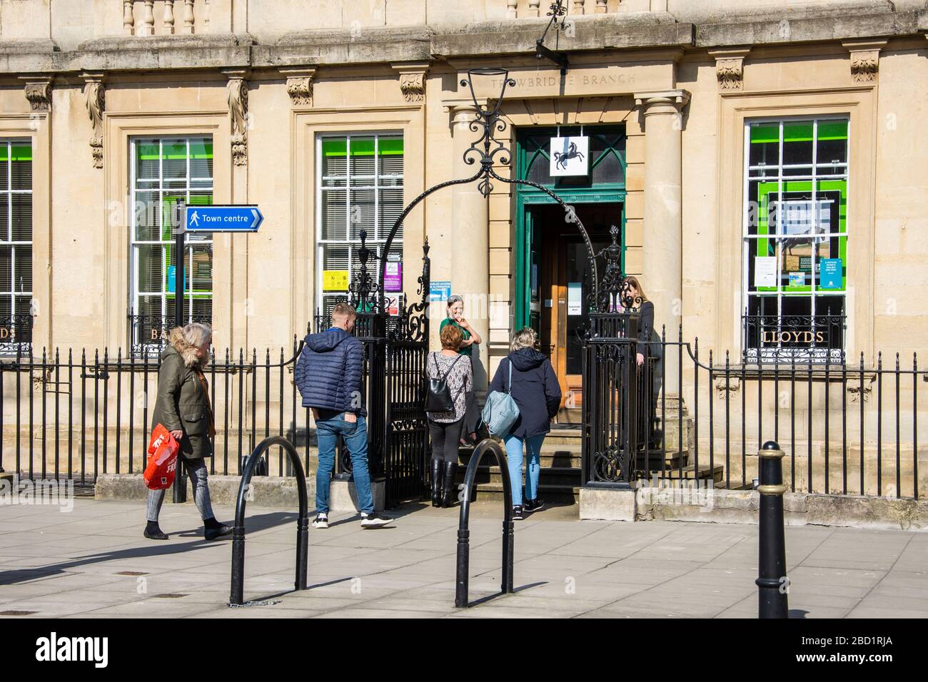 Kunden, die außerhalb der Lloyds Bank in Trowbrige Schlange stehen, werden während der Virusblockierung von Corona von Bankmitarbeitern überwacht Stockfoto