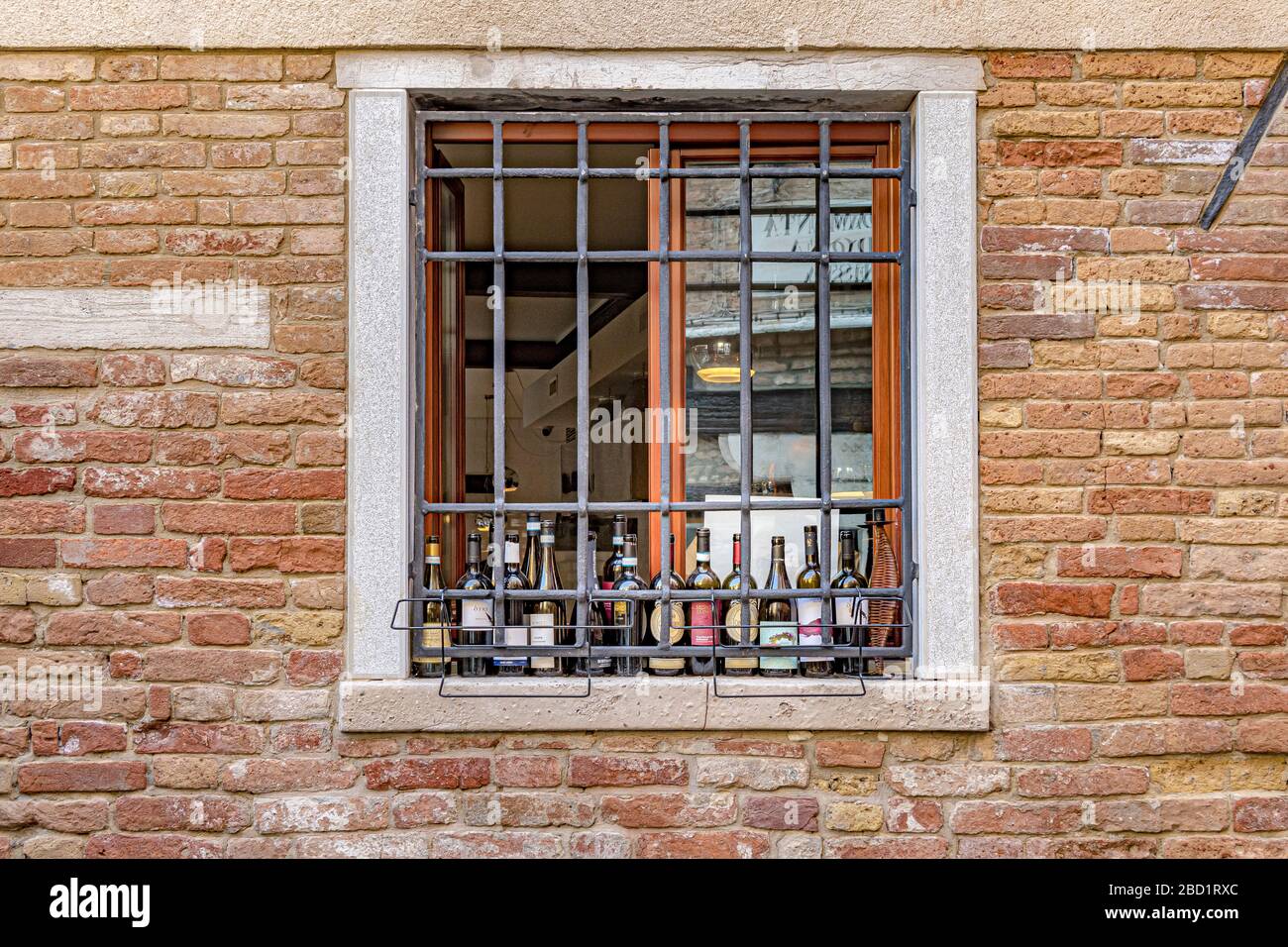 Glasflaschen sitzen auf einer Fensterbank hinter Metallfenster mit Sperrgitter in eine Ziegelmauer, Venedig, Italien Stockfoto