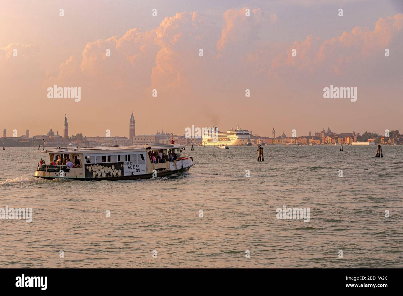 Ein Vaporetto, das Lido in Richtung Venedig verlässt, erscheint als großes Kreuzfahrtschiff in der Ferne, das die Lagune von Venedig, Venedig, Italien, überquert Stockfoto