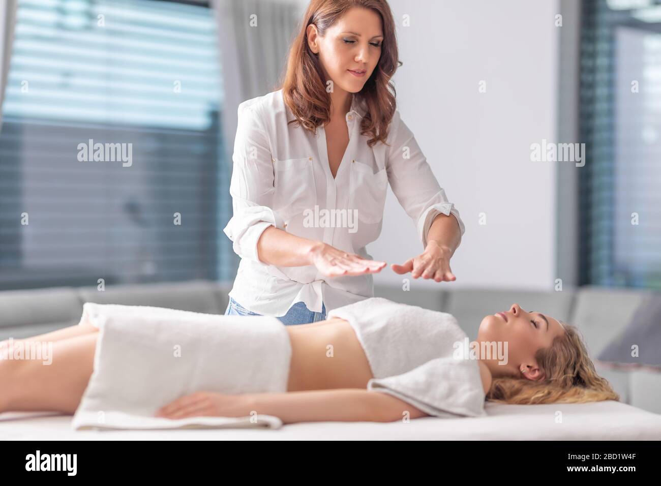 Fokussierter Reiki Heiler, der mit einer jungen schönen Frau in einem Wellness-Center therapiert wird. Stockfoto