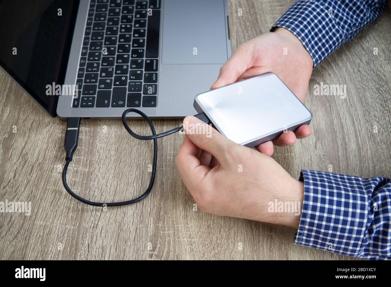 Männliche Hände in blau kariertem Hemd trennen eine externe Festplatte vom Laptop. Stockfoto