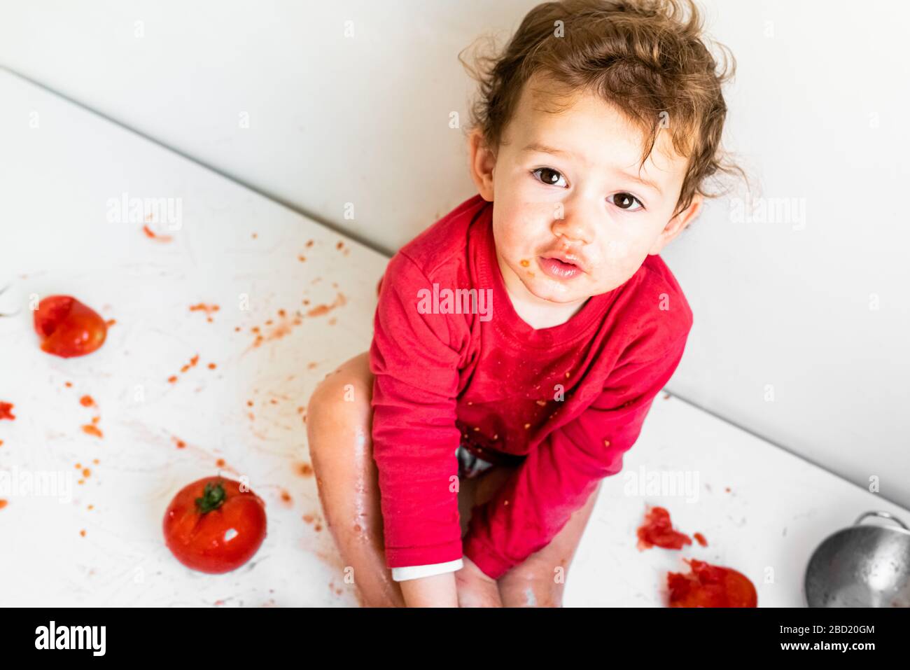 Baby sieht beim Kauen von Gemüse mit natürlichem Tomatensaft verschmutzt aus, isoliert auf Weiß. Stockfoto