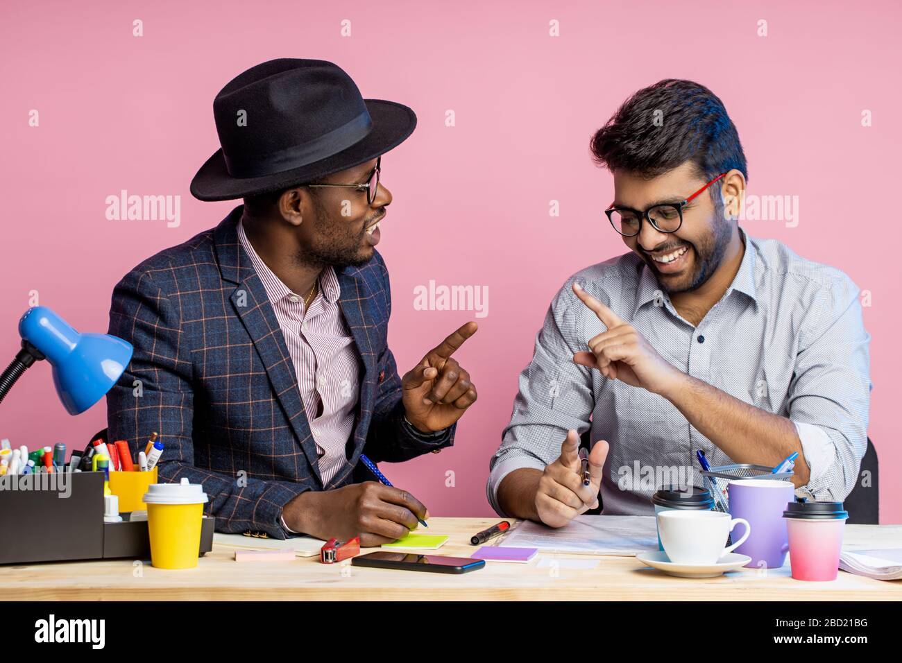 Zwei Kollegen arbeiten zusammen, diskutieren über neues Projekt, erstellen Finanzbericht, halten Stifte, sitzen am Büroschreibtisch, tragen formelle Kleidung, Brille, Stockfoto