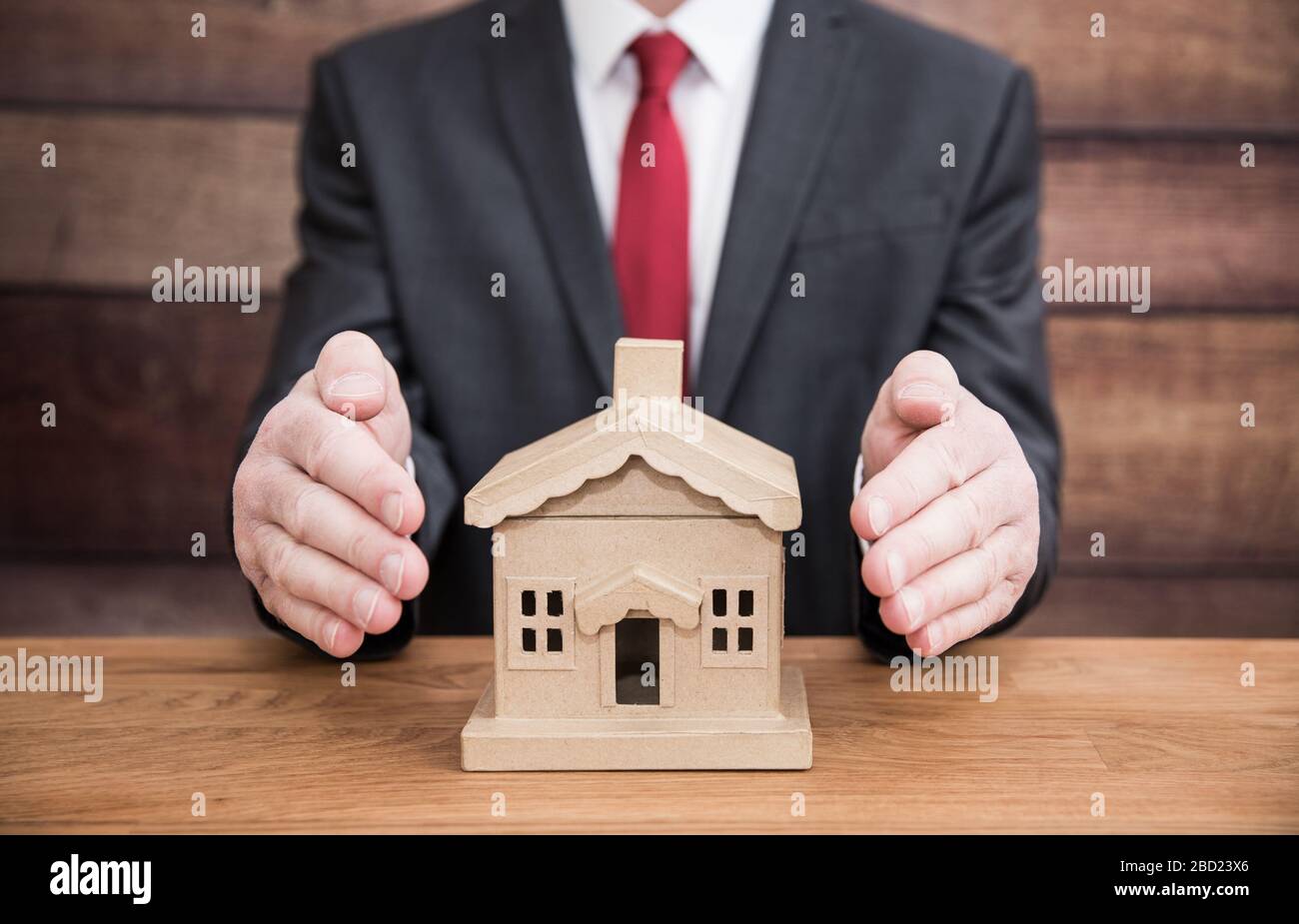 Ein Haus- oder Wohnungskonzept eines Geschäftsmannes wie eines Hypothekenanbieters oder einer Hausversicherung, die ein Haus oder Haus schützt, indem er seine Hände um es herum wickelt Stockfoto