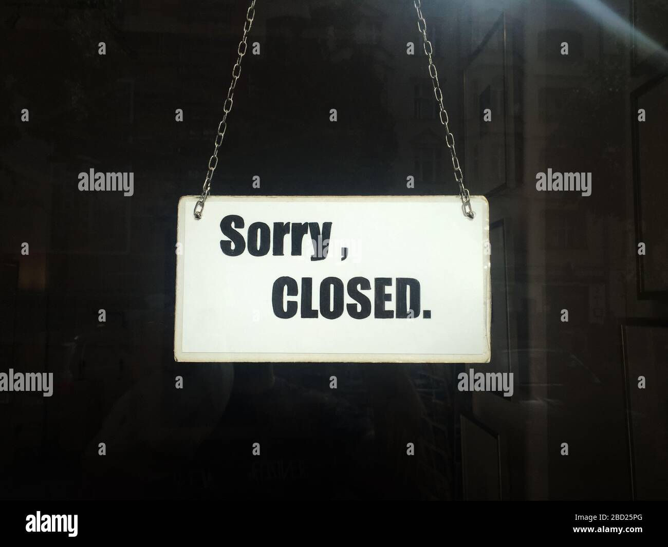 Herunterfahren. Geschlossenes Zeichen des kommerziellen Shops in Lockdown mit Sorry geschlossen Typografie auf Karton mit Metallbändern hängen im Schaufenster Stockfoto