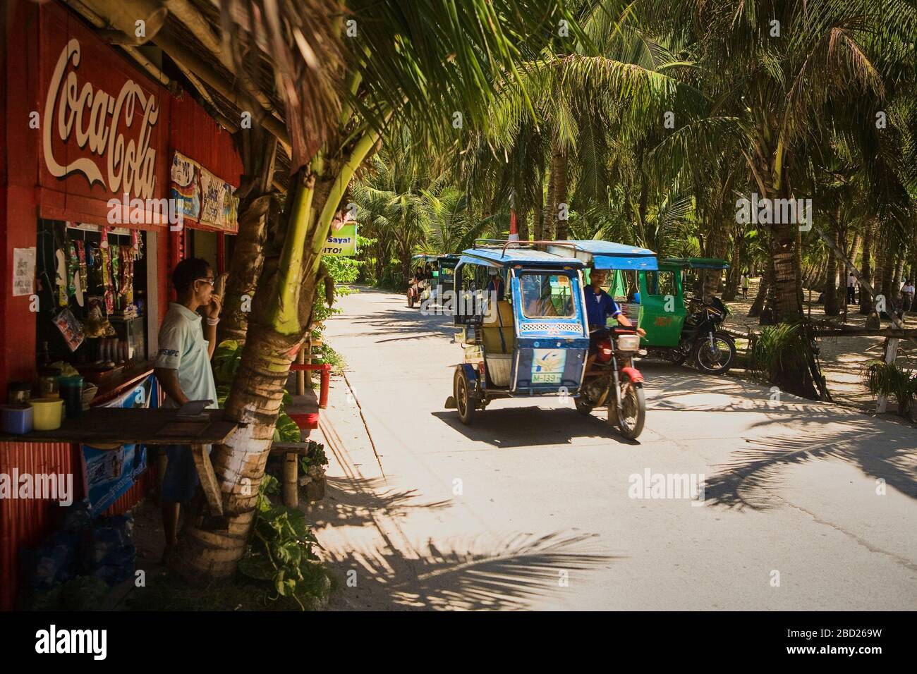 Ein Tuk Tuk passiert einen Kiosk in einem Palmenwald auf Boracay. Stockfoto