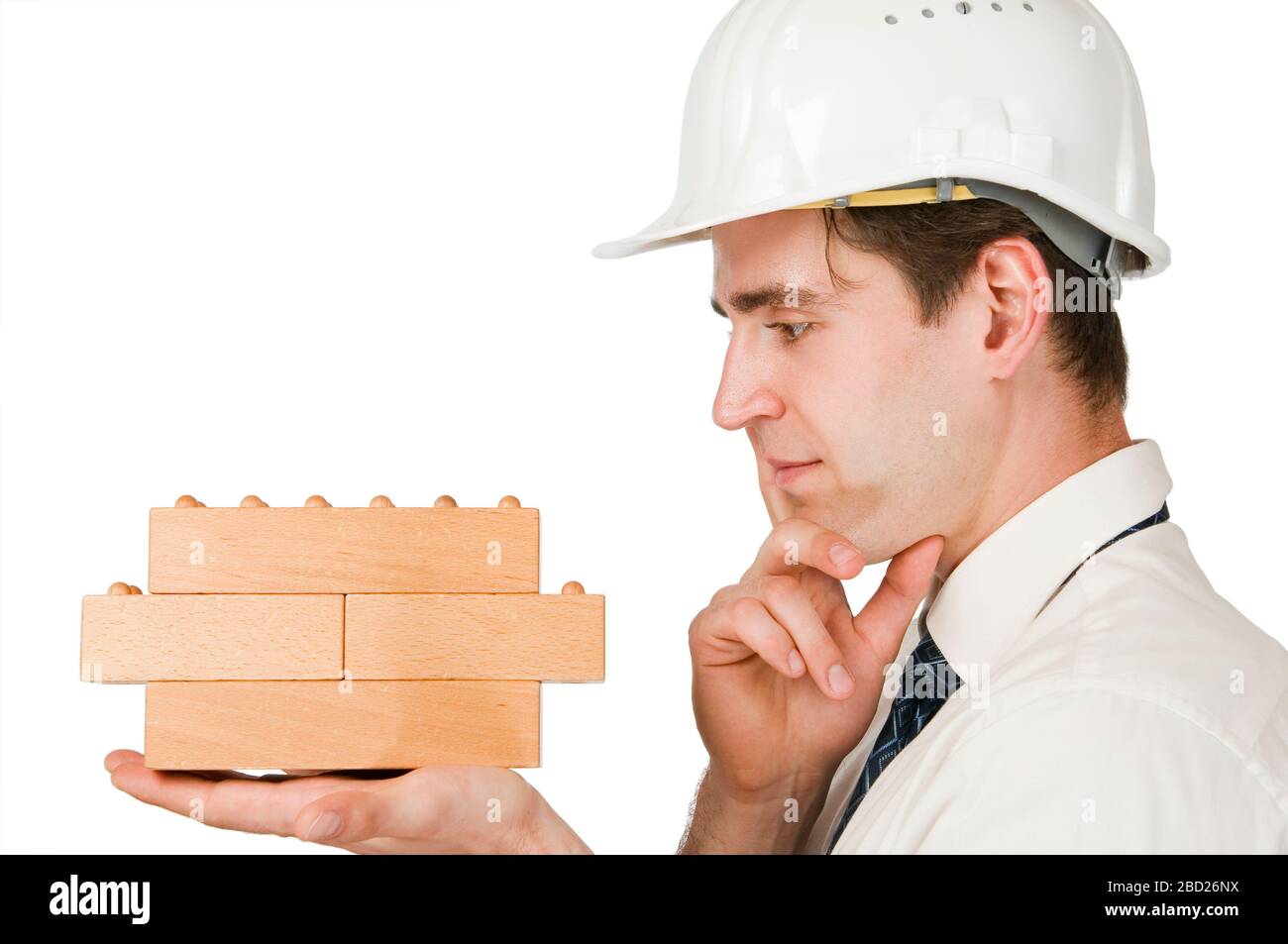 Kopf-und-Schulteransicht eines jungen Mannes im Profil mit weißem Hemd, Krawatte und weißem Baustellenhelm, der nachdenklich auf die Holzblöcke blickt. Stockfoto