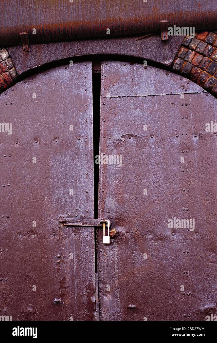 Architektur. Eisenbahnbogen aus viktorianischem Backstein. Rostige, mit einem Vorhängeschloss verschlossene Tür. Stockfoto