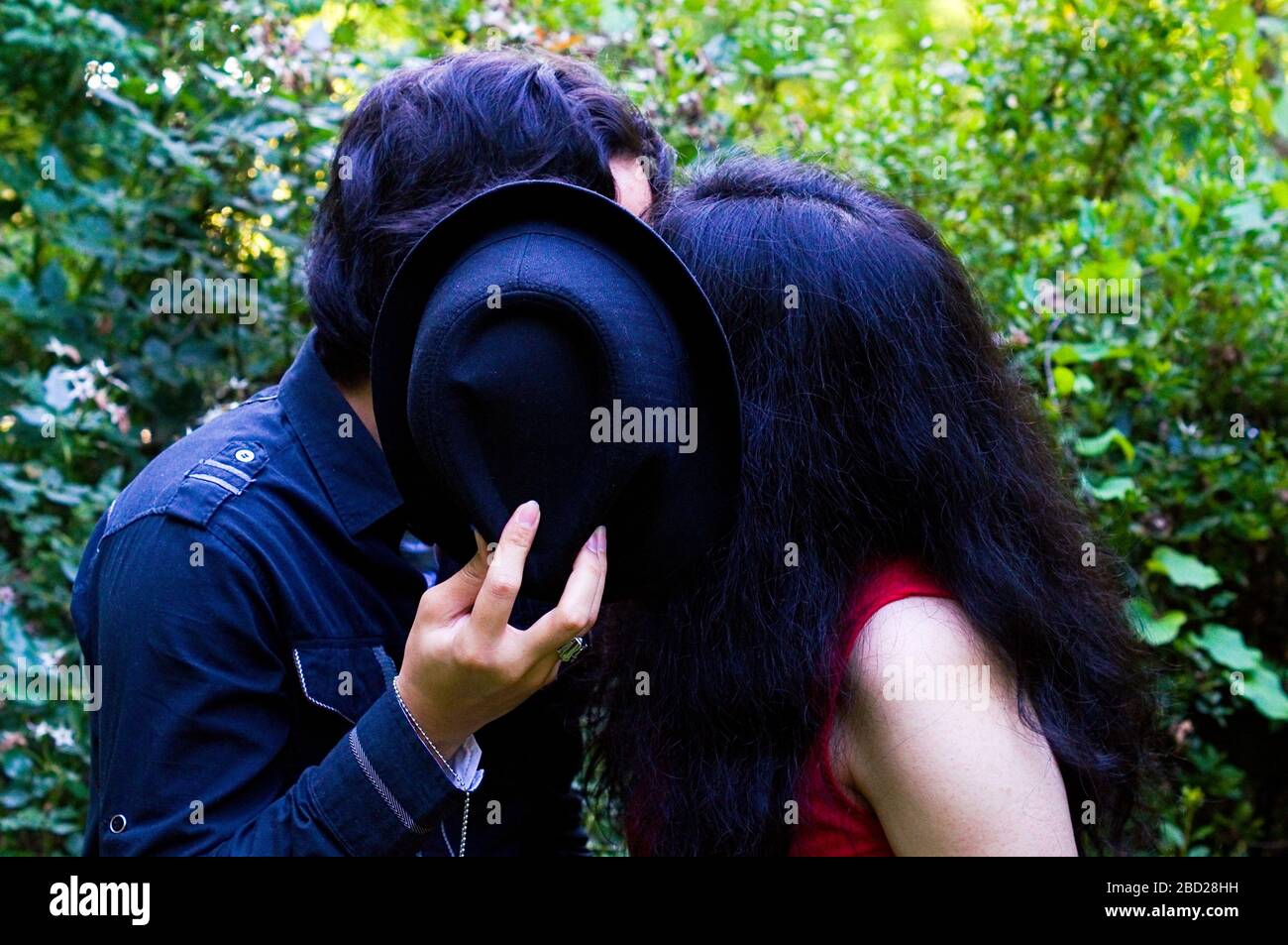 Freund und Freundin küssen, während sie ihre Gesichter mit einem Hut verstecken Stockfoto