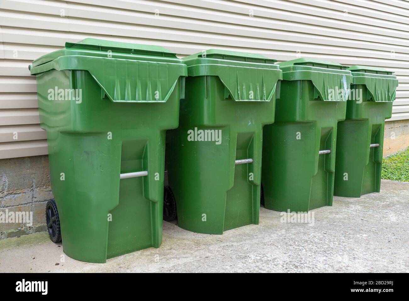 Der horizontale Schuss aus vier grünen Kunststoff-Abfallbehältern verläuft gegen die Außenwand einer Eigentumswohnung. Stockfoto