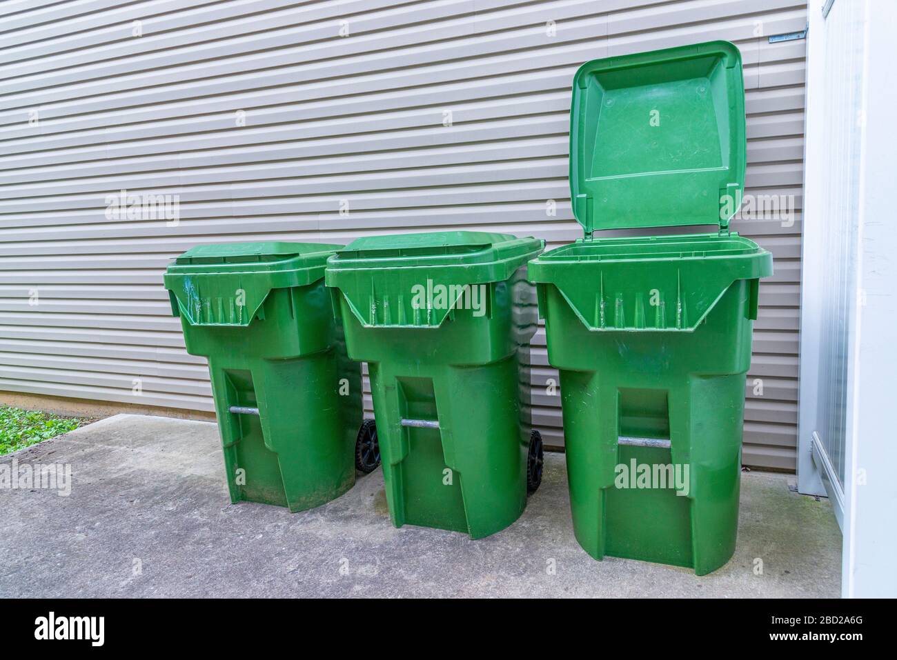 Der horizontale Schuss von drei grünen Kunststoff-Abfallbehältern verläuft gegen die Außenwand einer Eigentumswohnung. Man hat seinen Deckel oben. Stockfoto