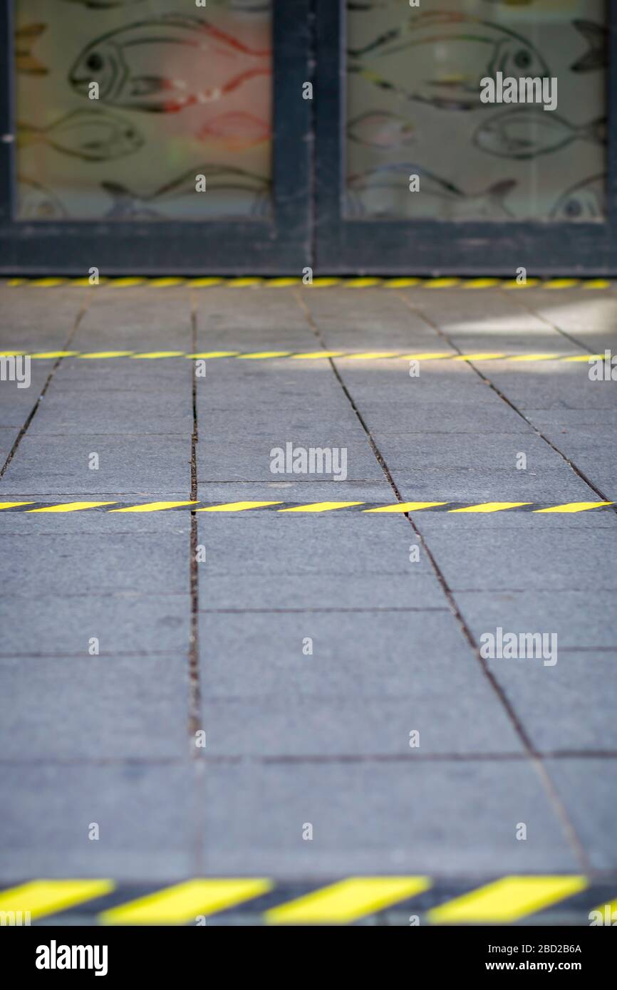 Markierungen auf dem Bürgersteig, damit die Menschen stehen, während sie vor einem Geschäft Schlange stehen, um soziale Distanzen durch das Coronavirus zu leiten Stockfoto