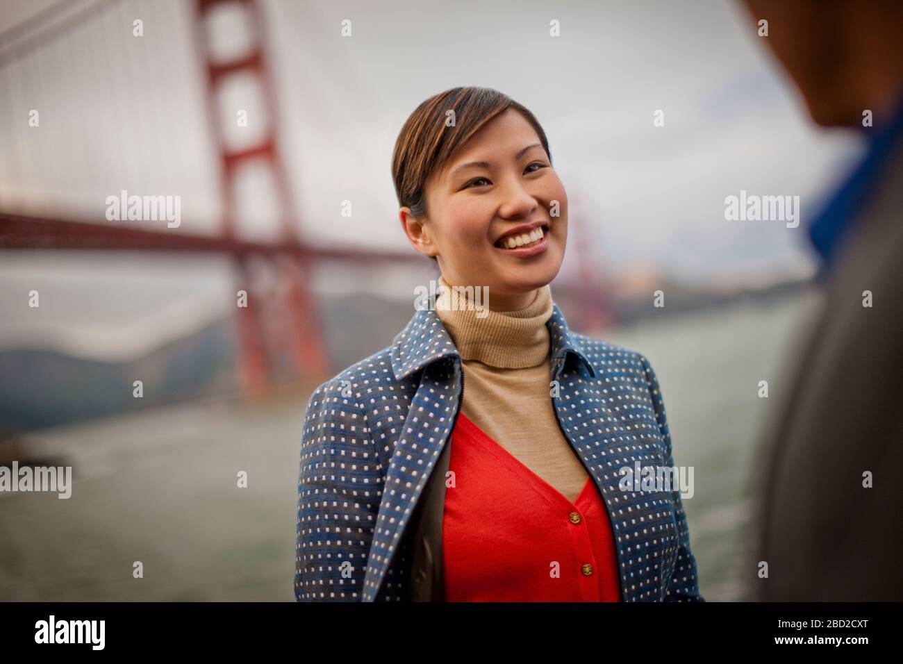 Lächelnde junge Frau spricht mit einem Freund von der Golden Gate Bridge in San Francisco, USA. Stockfoto