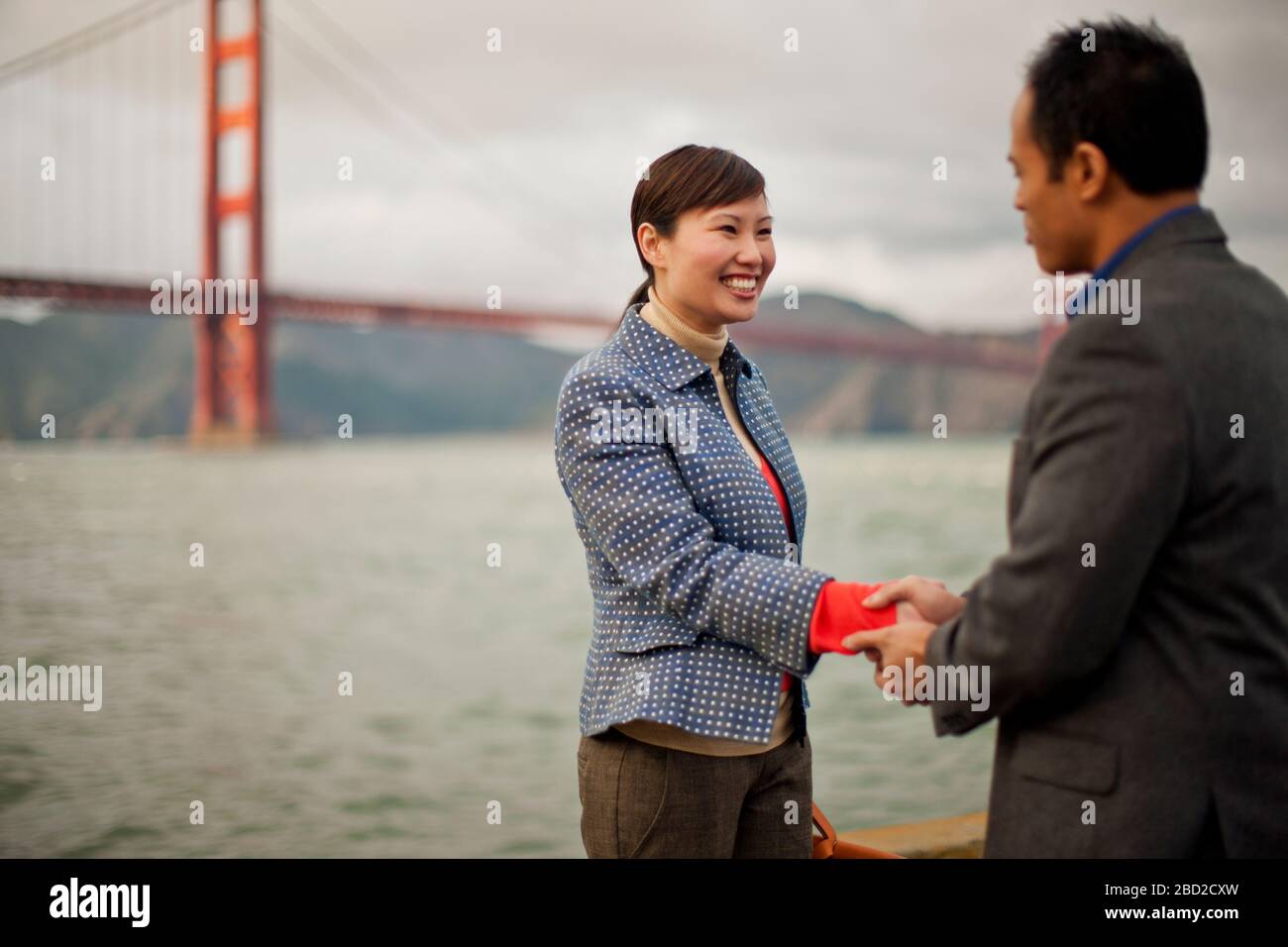 Lächelnde junge Frau versiegelt einen Geschäftsabschluss mit einem Handschlag vor der Golden Gate Bridge. Stockfoto