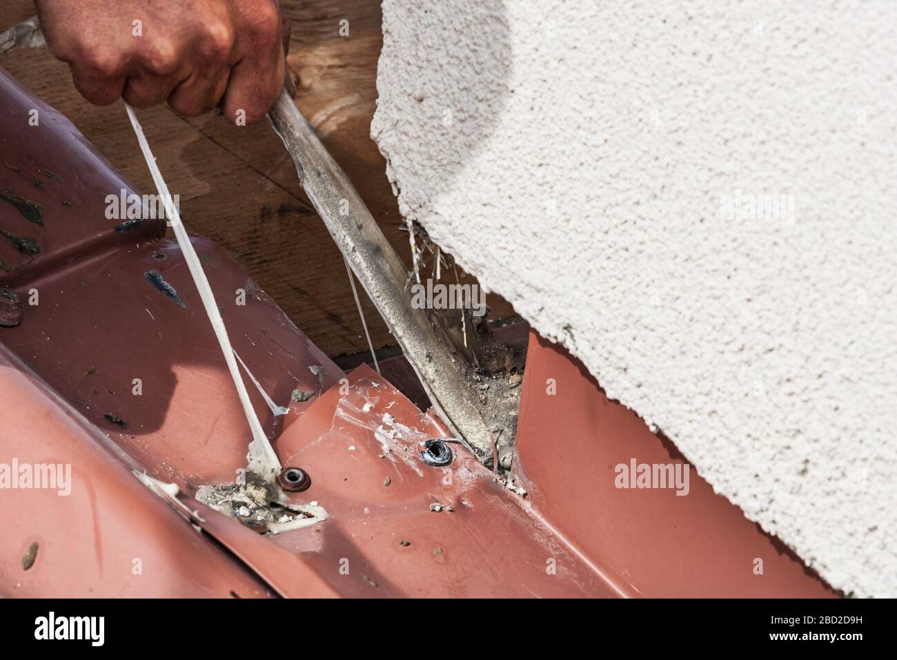 Ein Dachdecker entfernt Klebstoff bei der Reparatur von Wellpappendach Stockfoto