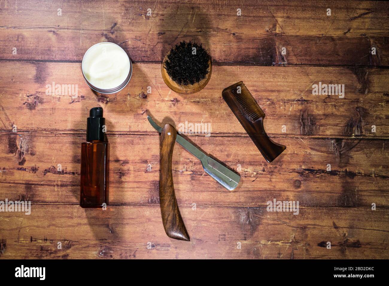 Eine Auswahl an Bartpflegeprodukten für Männer, darunter Öl, Wachs und eine Bürste, die vor einem Holzhintergrund geschossen wurden Stockfoto
