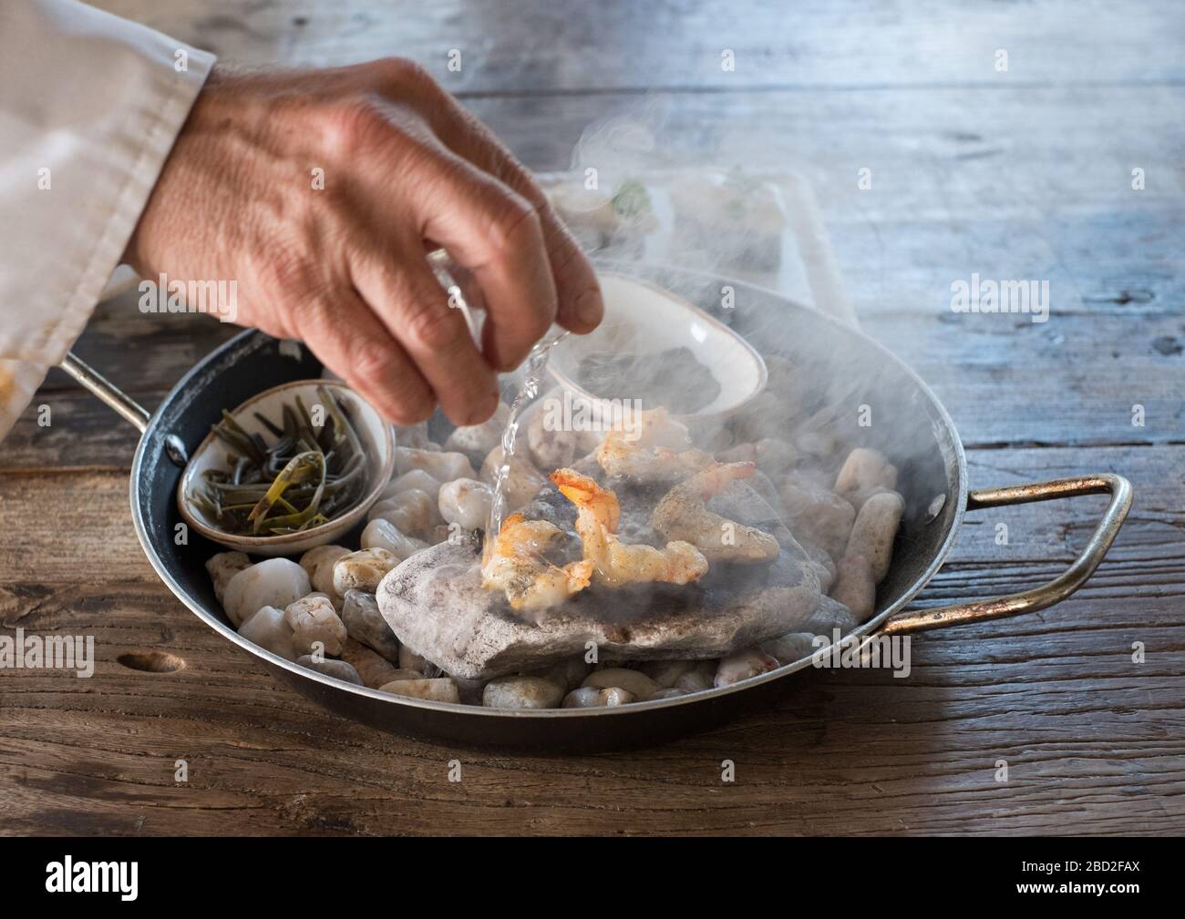 Küchenchef Giannis Baxevanis gießt Ouzo über Garnelen, die auf Kieselsteinen zubereitet werden, mit weißer Tarama-Mousse im Six Keys Restaurant auf der griechischen Halbinsel Pelion Stockfoto